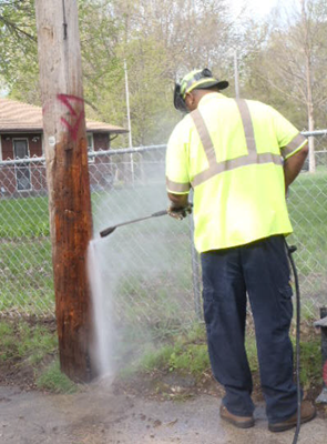 person using pressure washer to remove graffiti from telephone pole