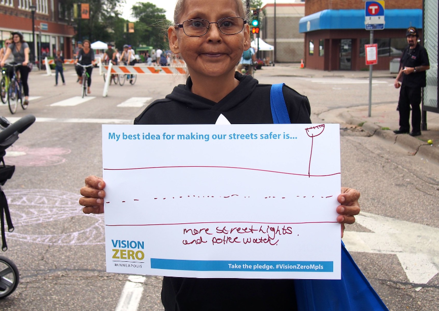 Person holding sign that says "My best idea for making our streets safer is: More street lights and police watch.