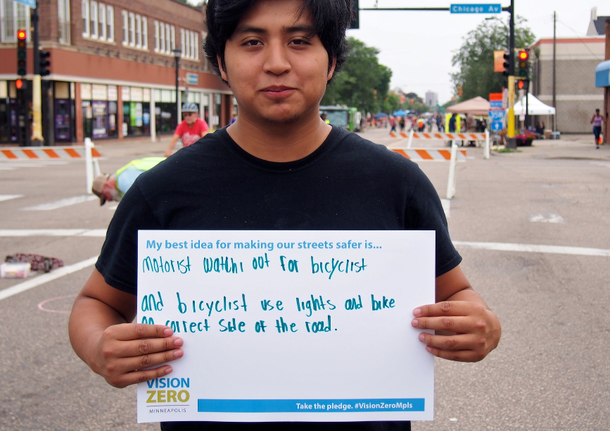 Person holding sign: My best idea for making our streets safer: Motorist watch out for bicyclist. Bicyclist use lights & bike on correct side of road.