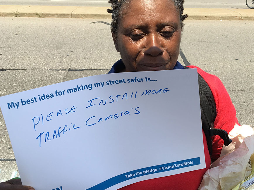 A person holding a sign that says please install more traffic cameras.