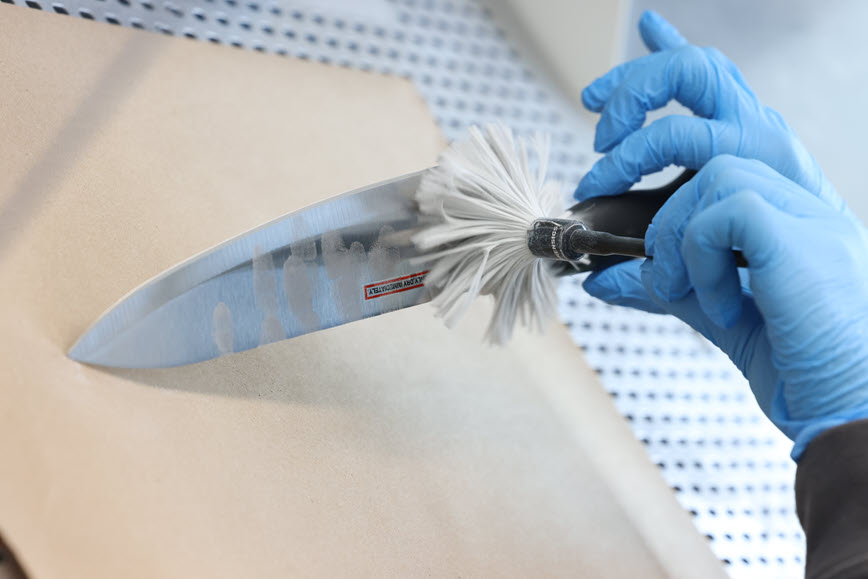 Gloved hands dusting for fingerprints on a knife