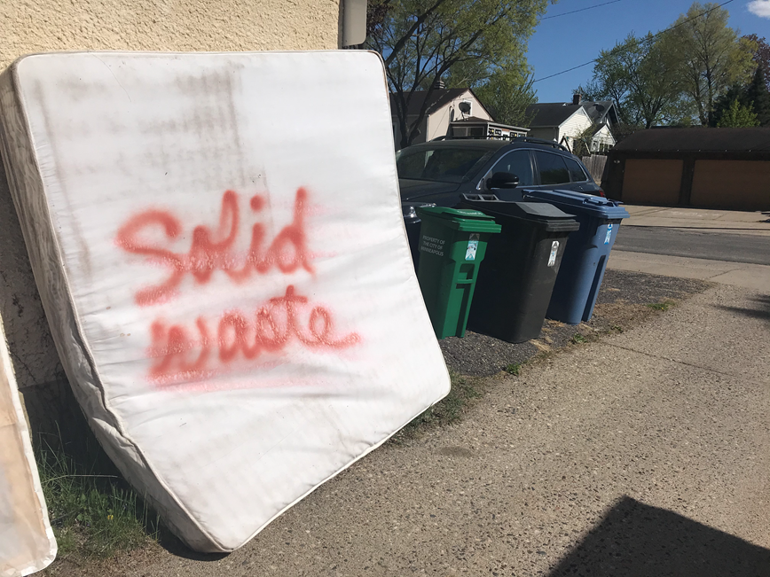 mattress labeled 'for solid waste' set out by carts for pickup