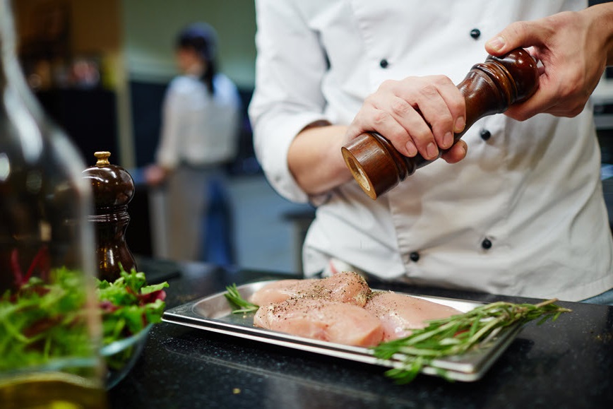 Chef putting seasoning raw chicken in restaurant kitchen