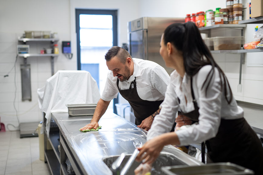 Two people in restaurant kitchen sanitizing food surface