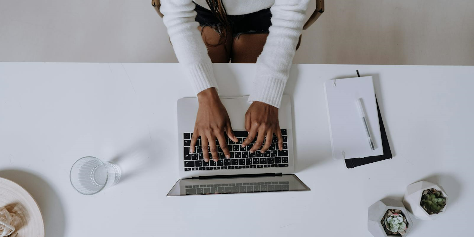 Person typing on laptop with notepad on desk