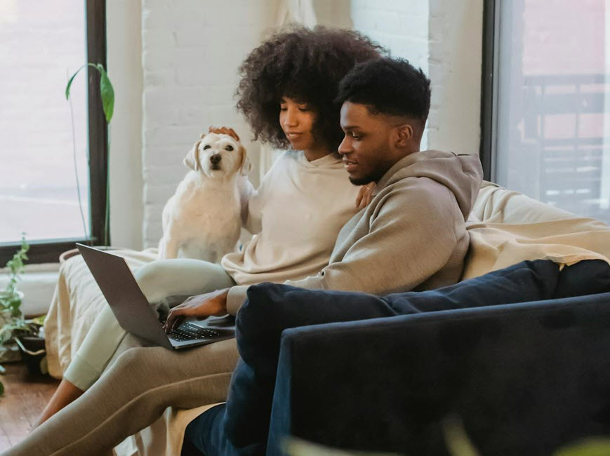 Two people on couch using laptop with dog nearby