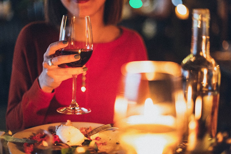 person holding wine glass with food on the table