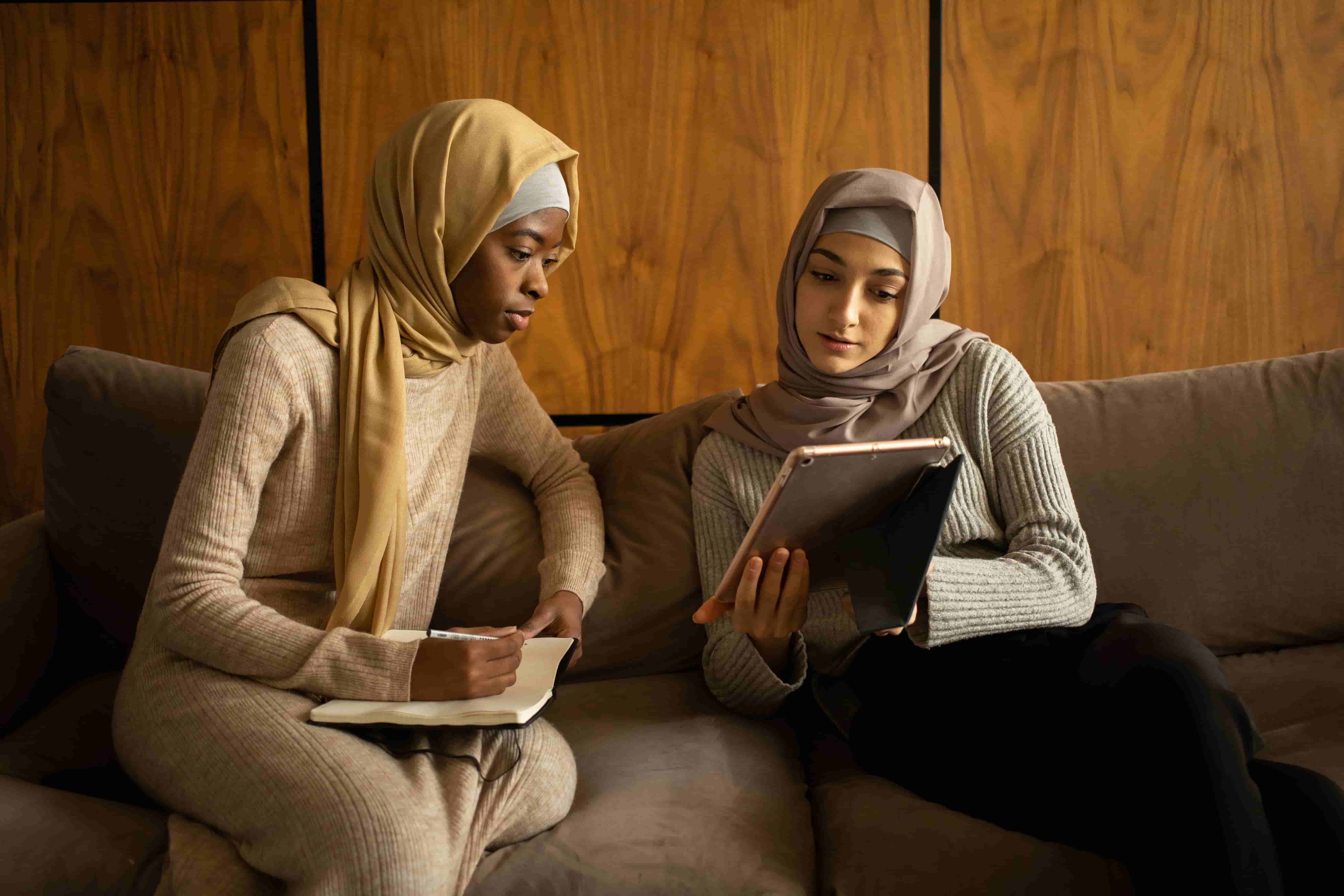 Two people wearing hijabs reading a tablet